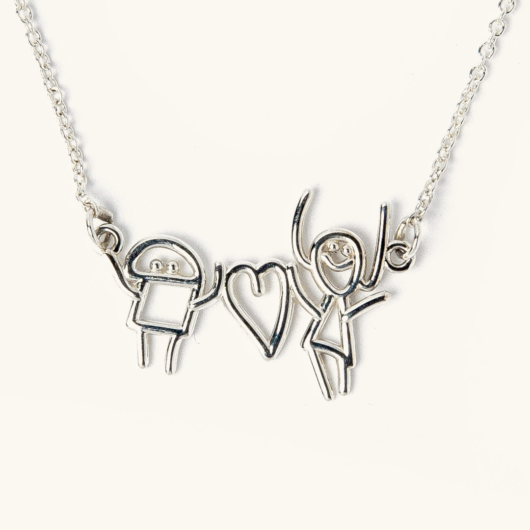 Custom silver necklace featuring two child-like drawing characters holding a heart, transformed into a pendant on a chain.