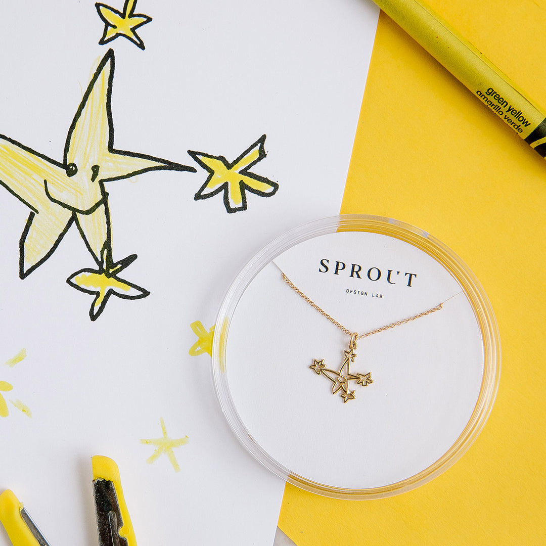 Gold custom artwork necklace with star pendant, displayed with child’s star drawing and markers.