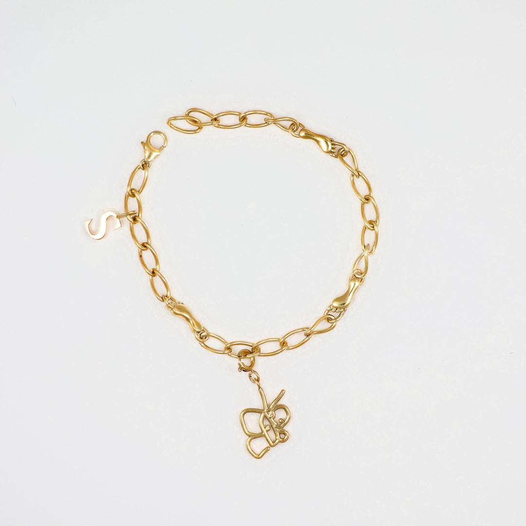 Gold chain bracelet with butterfly charm and small “S” detail on a white background